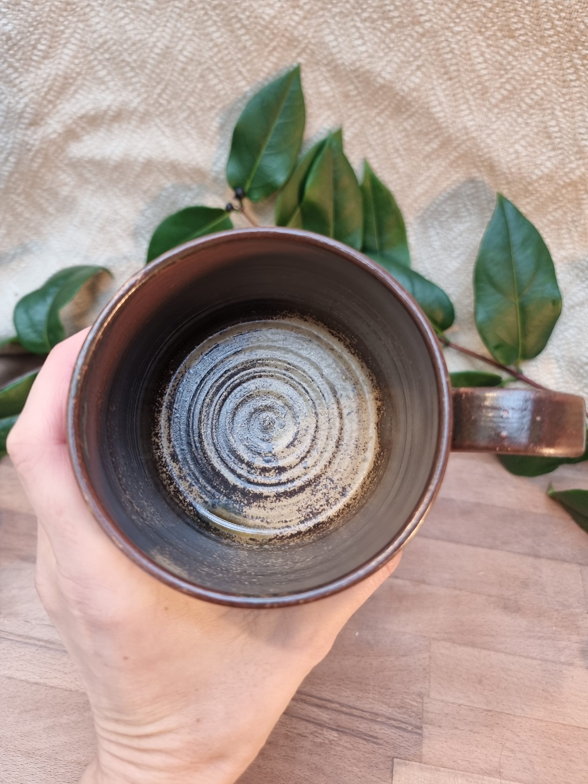 Brown mug from above, over a wooden table and greenery.