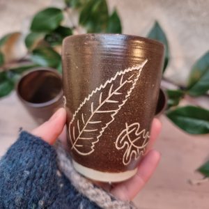 brown beaker with white leaves on wooden bench with greenery