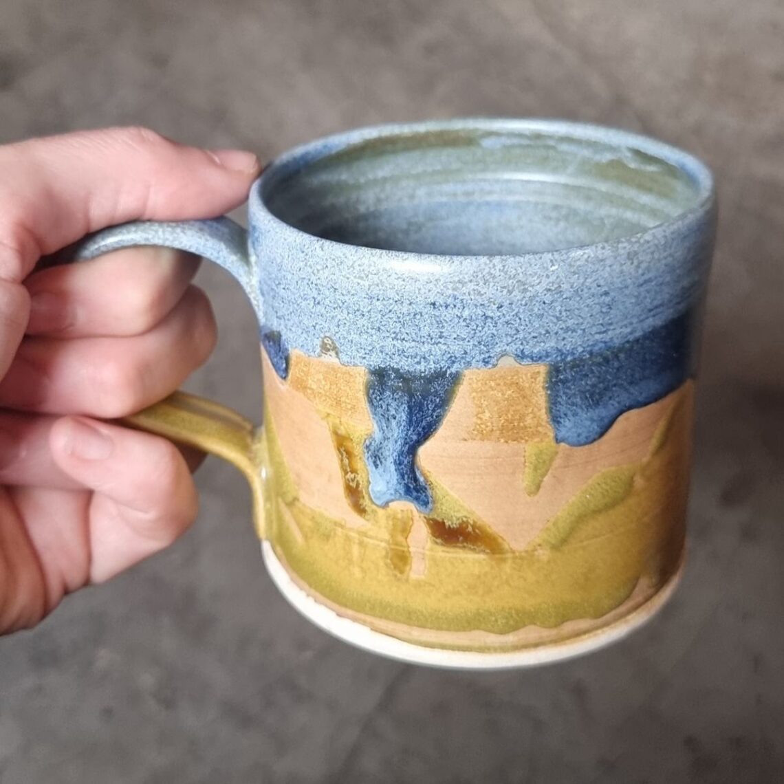 yellow and blue mug held in hand on grey background