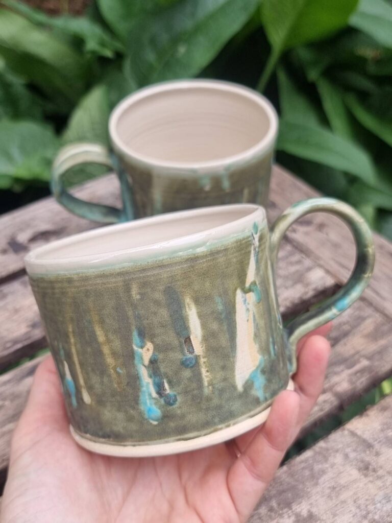 greeny white mug on wooden table with greenery behind